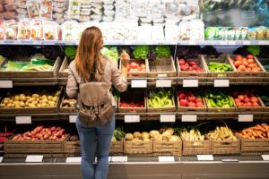 frau steht vor gemueseregal im supermarkt