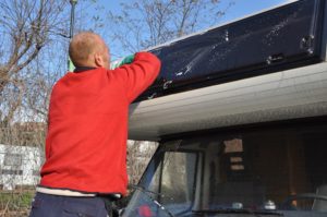 ein mann poliert eine acrylglasscheibe an seinem wohnmobil