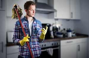 ein junger mann schaut beim putzen auf sein smartphone