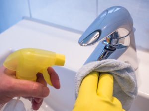 Hand putzt mit Lappen und Sprühflasche einen Wasserhahn