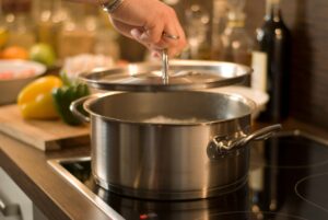 Eine Person hält den Deckel eines Kochtopfs, in dem Wasser erhitzt wird, in der Hand.