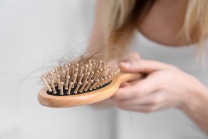 eine frau haelt eine haarbuerste mit haaren in der hand