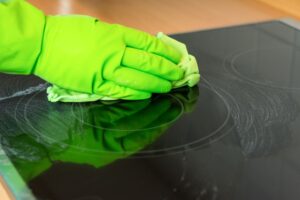 Eine Person mit einem grünen Handschuh reinigt ein Ceranfeld.