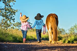 Junge und Mädchen laufen als Cowboy und Cowgirl verkleidet mit Ponny