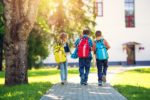 Kinder mit Rucksäcken vor der Schule