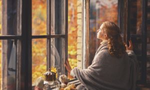 Frau vor offenem Fenster im Herbst