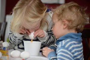 zwei kinder pusten gemeinsam ostereier aus