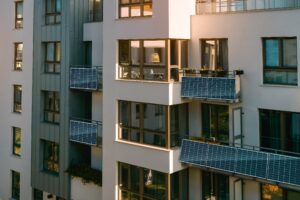 Eine Wand eines Wohnhauses mit Wohnungen mit mehereren Solarpanels auf den meisten Balkonen.