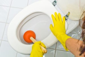 Eine verstopfte Toilette wird gereinigt. Mit gelben Latex Handschuhen.