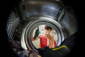 Frau hält sich die Nase beim Blick in die Waschtrommel weil Wäsche nach Waschen stinkt